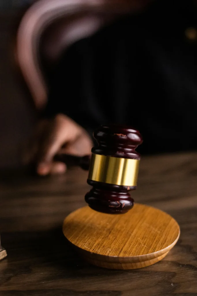 A hand holding a wooden gavel above a round wooden sound block on a table, suggesting a judicial or legal setting.